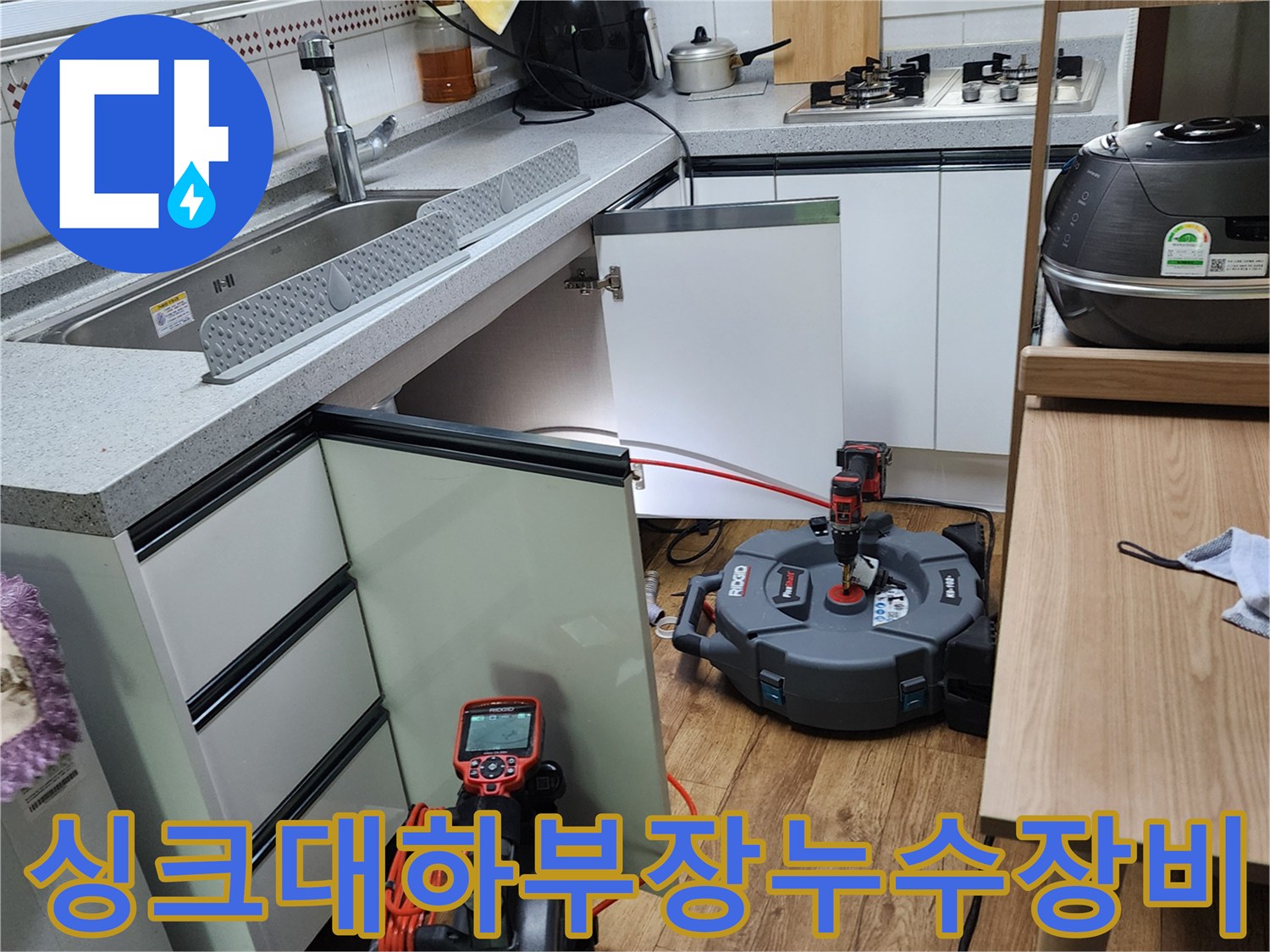 주방 싱크대 하부장 아래에서 정밀 누수 탐지 장비를 사용하여 배관 상태를 점검하는 모습입니다.