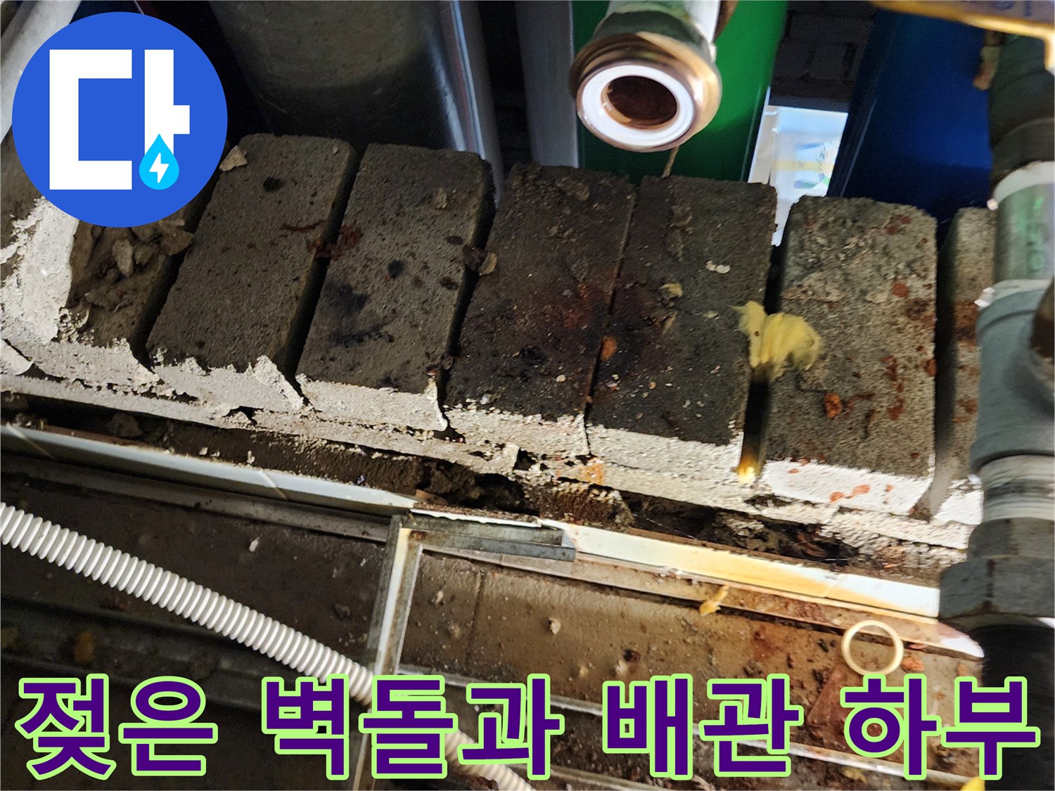 물기가 스며든 벽돌 틈새와 배관 하단부를 촬영한 사진입니다.