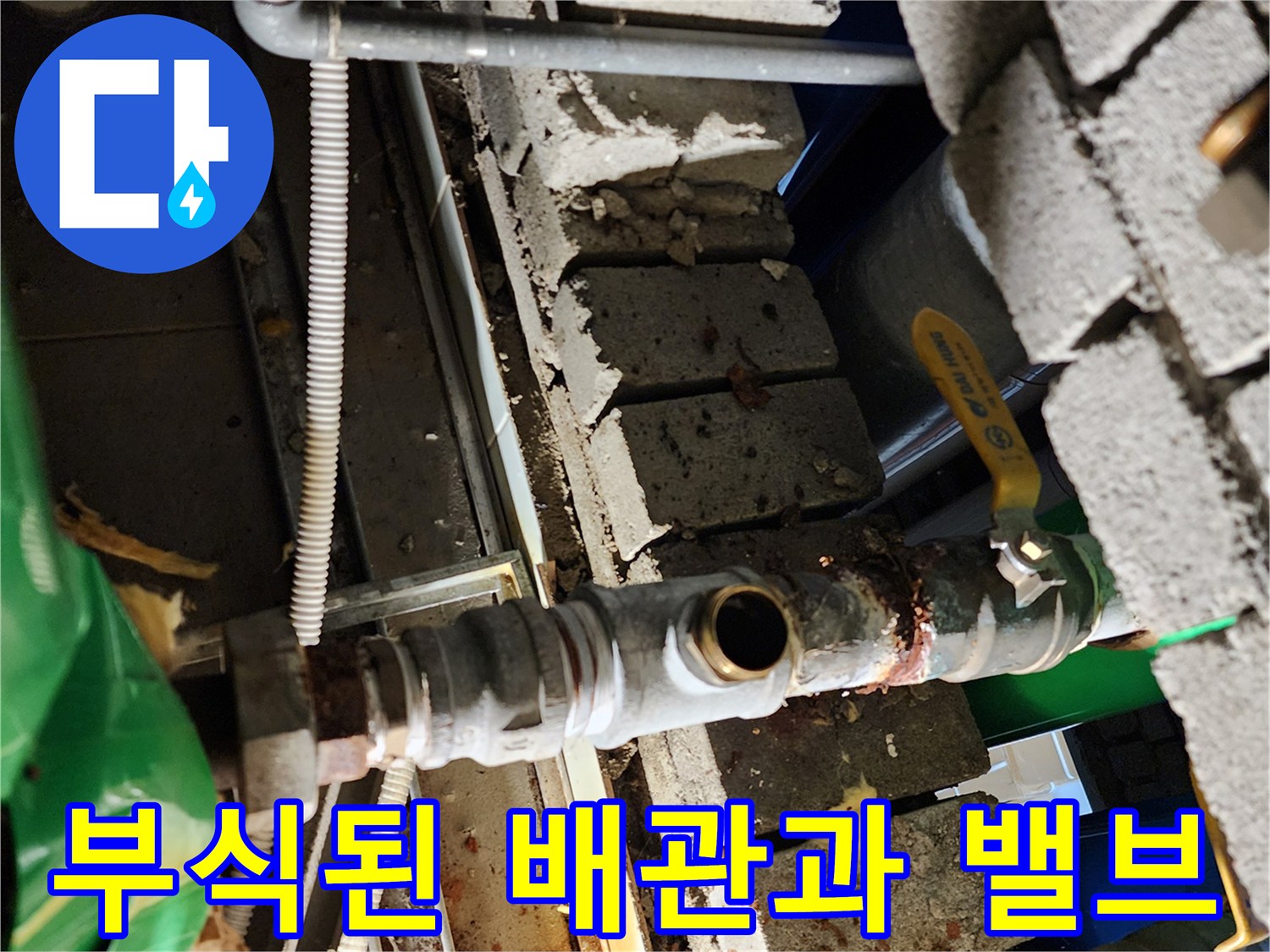 벽돌 사이 부식된 금속 배관과 노란색 손잡이 밸브 모습