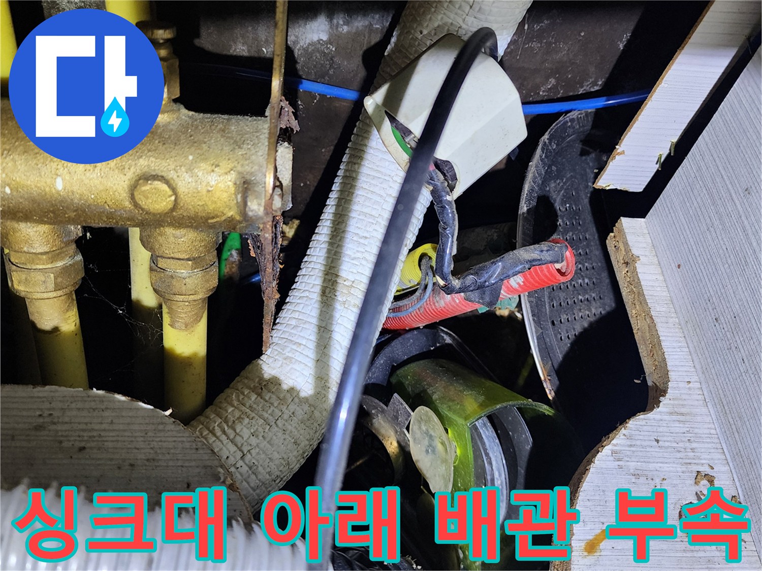 싱크대 하부의 황동색 밸브와 흰색 주름관이 복잡하게 연결된 모습입니다.