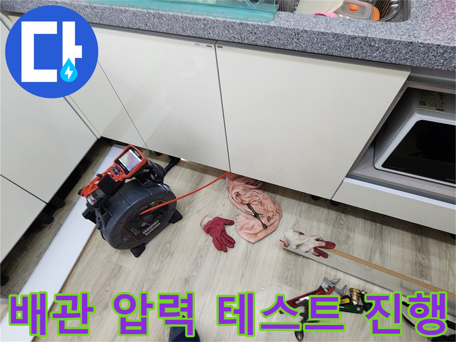 싱크대 하단 공간에 놓인 디지털 압력계와 누수 탐지용 장비의 모습