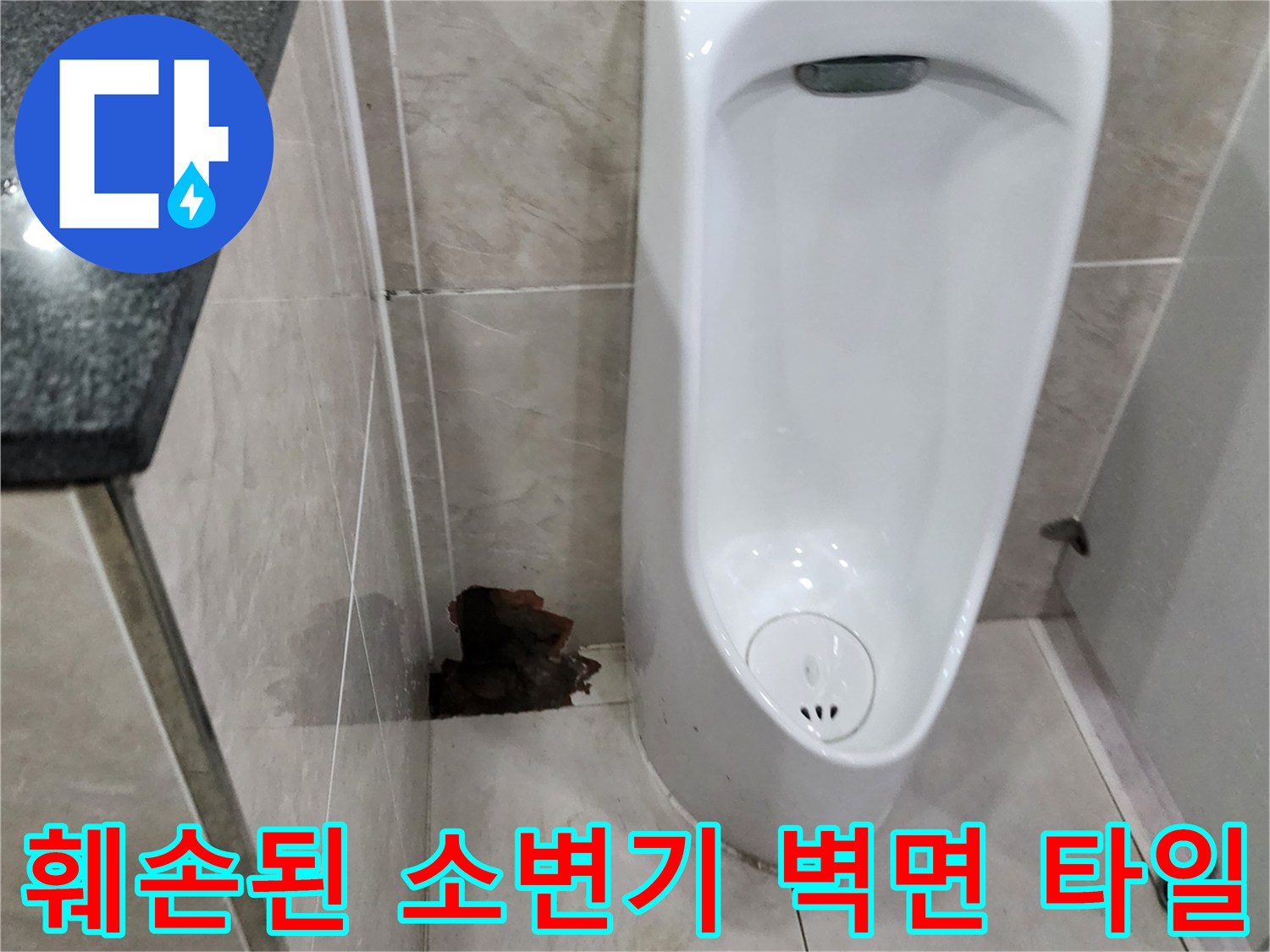 소변기 주변의 타일이 떨어져 나가 배관 부위가 노출된 상태입니다.