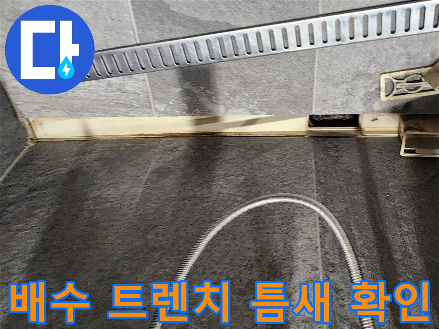 욕실 바닥 배수 트렌치와 타일 경계면의 균열을 근접 촬영한 사진입니다.