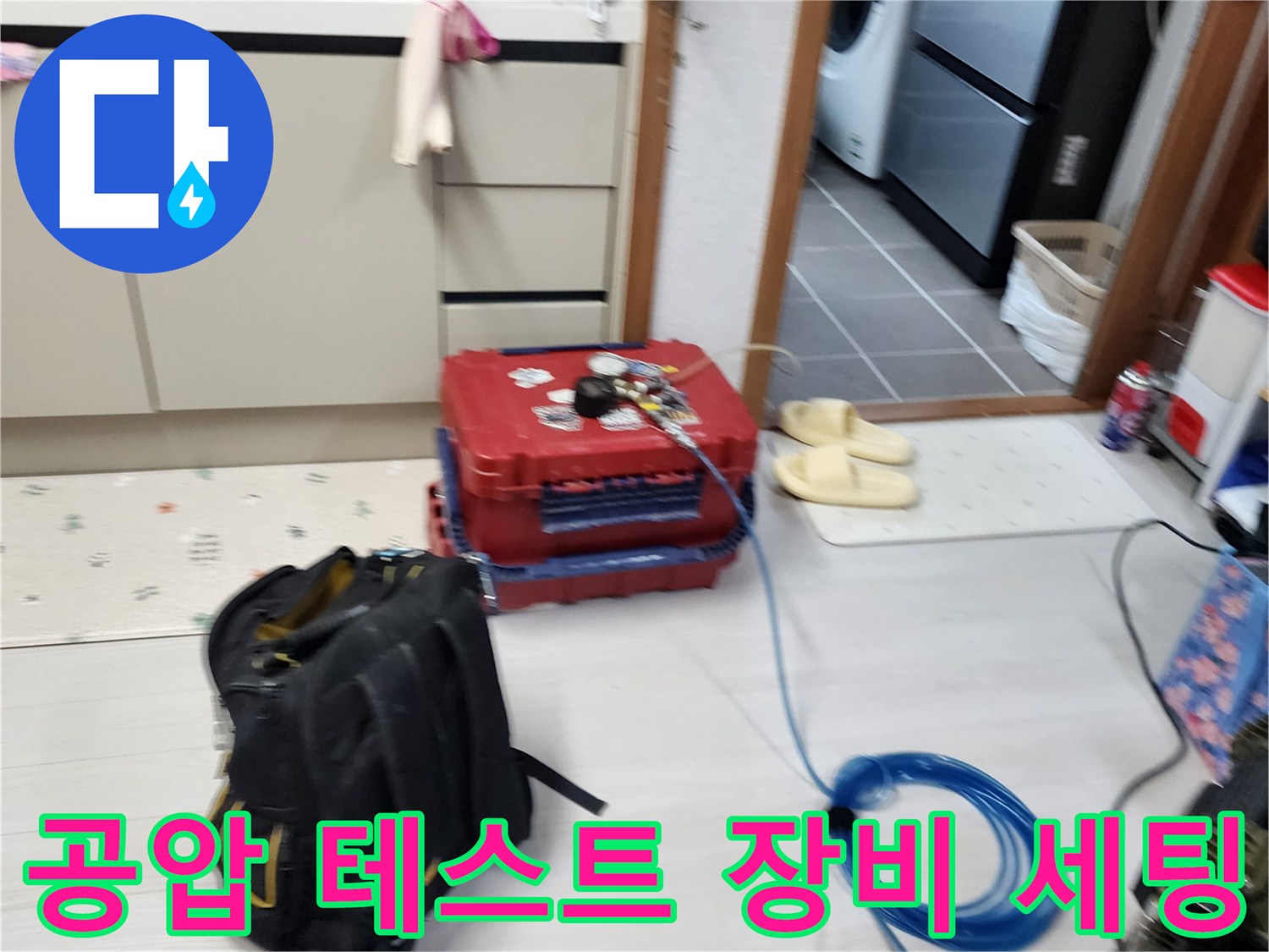 주방 바닥에 놓인 빨간색 압력계 케이스와 파른색 에어 호스 연결부