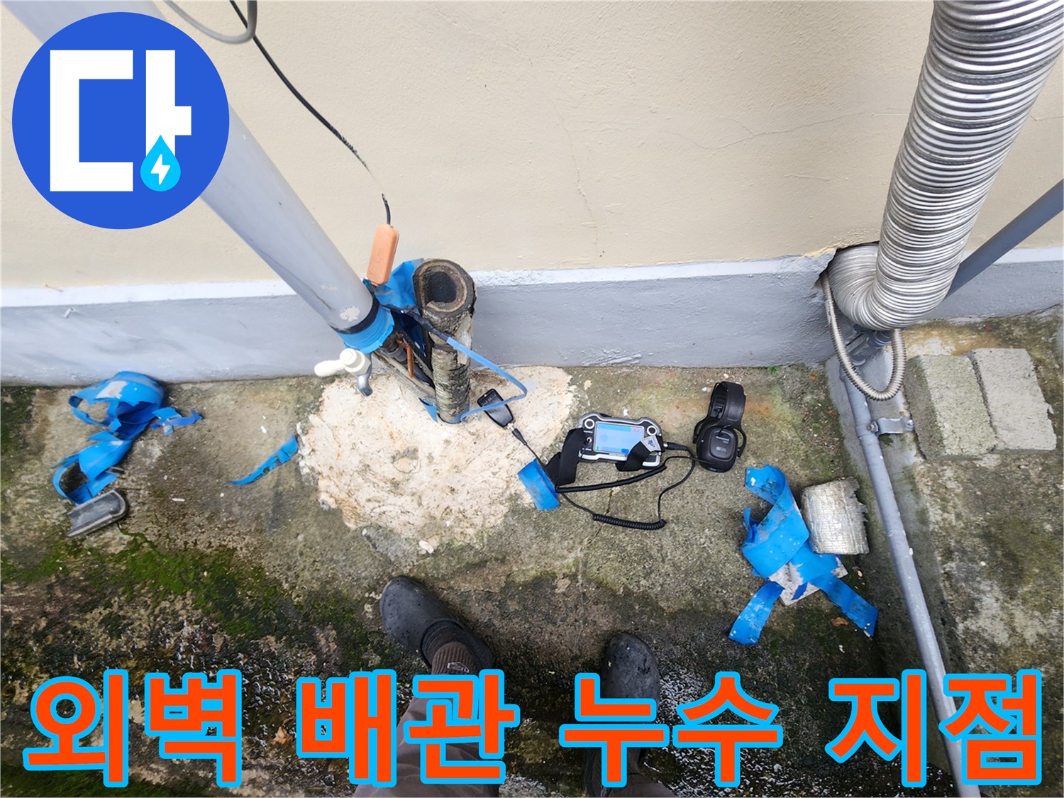 건물 외벽 하단 배관 주변의 젖은 토양과 탐지 장비 모습