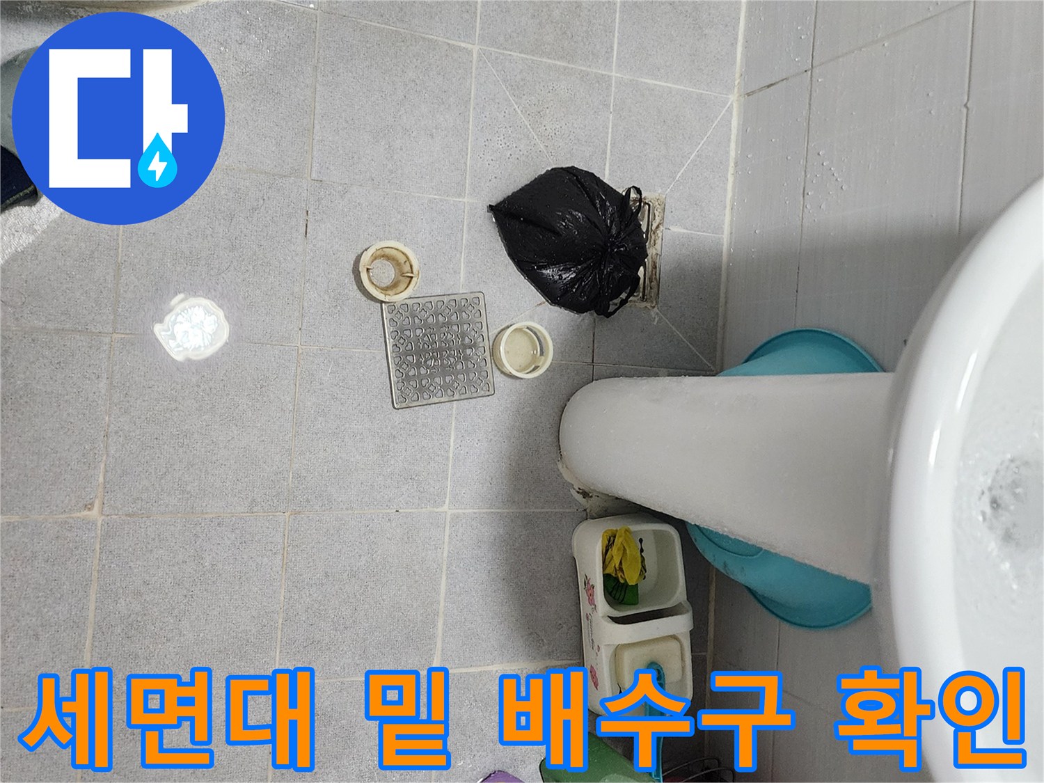 욕실 세면대 하단부의 배수구 부품과 바닥 타일 근접 촬영