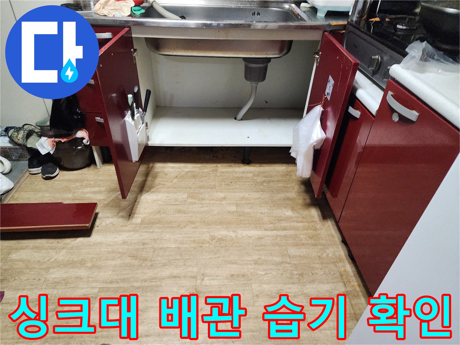 열린 싱크대 하부장 내부의 젖은 바닥과 배관 모습
