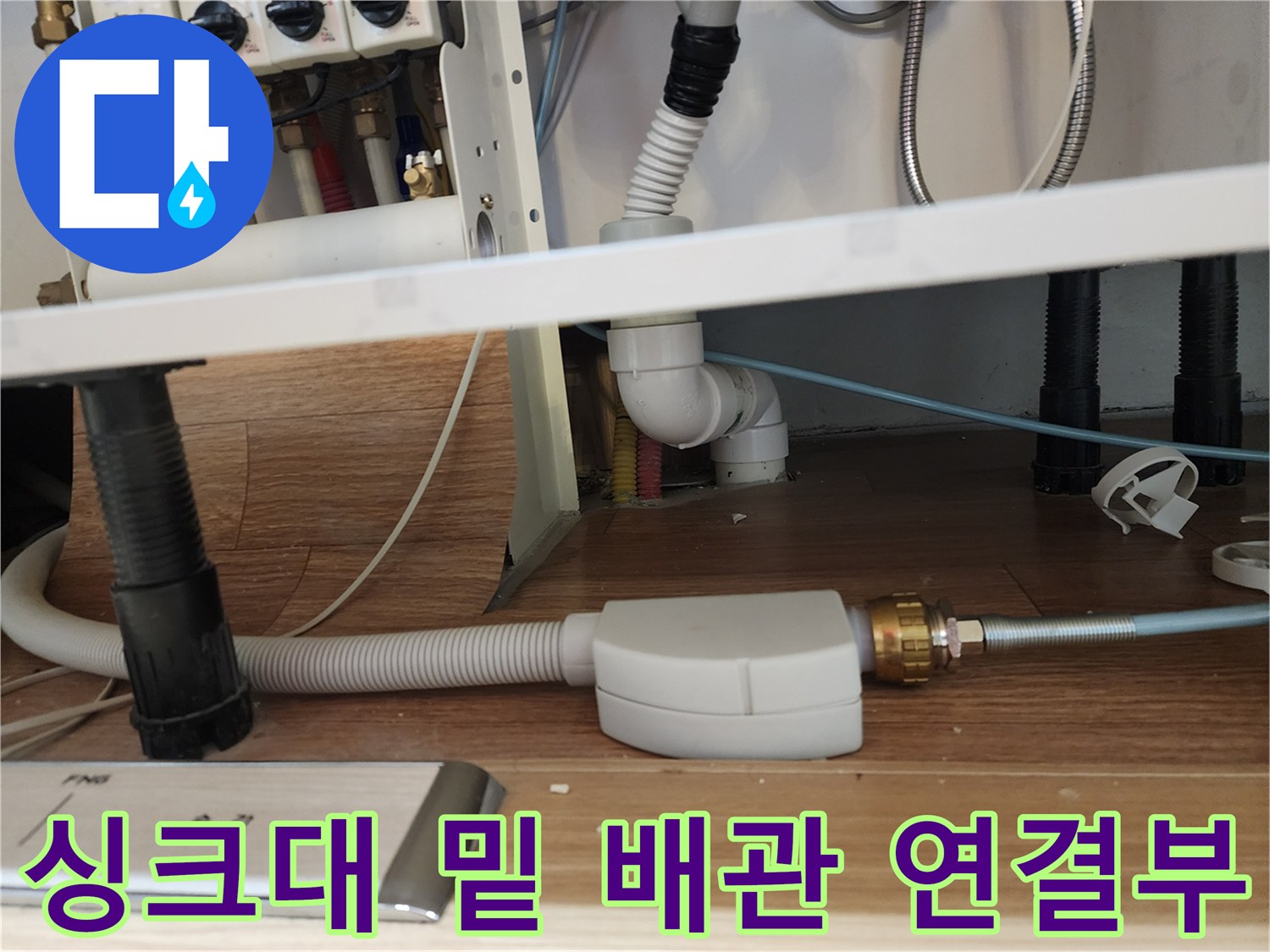 하얀색 플라스틱 관과 금속 부품이 연결된 싱크대 하부 사진