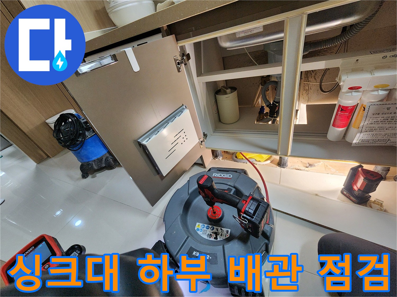 주방 싱크대 하부장 내부의 배수 배관과 작업용 장비 모습