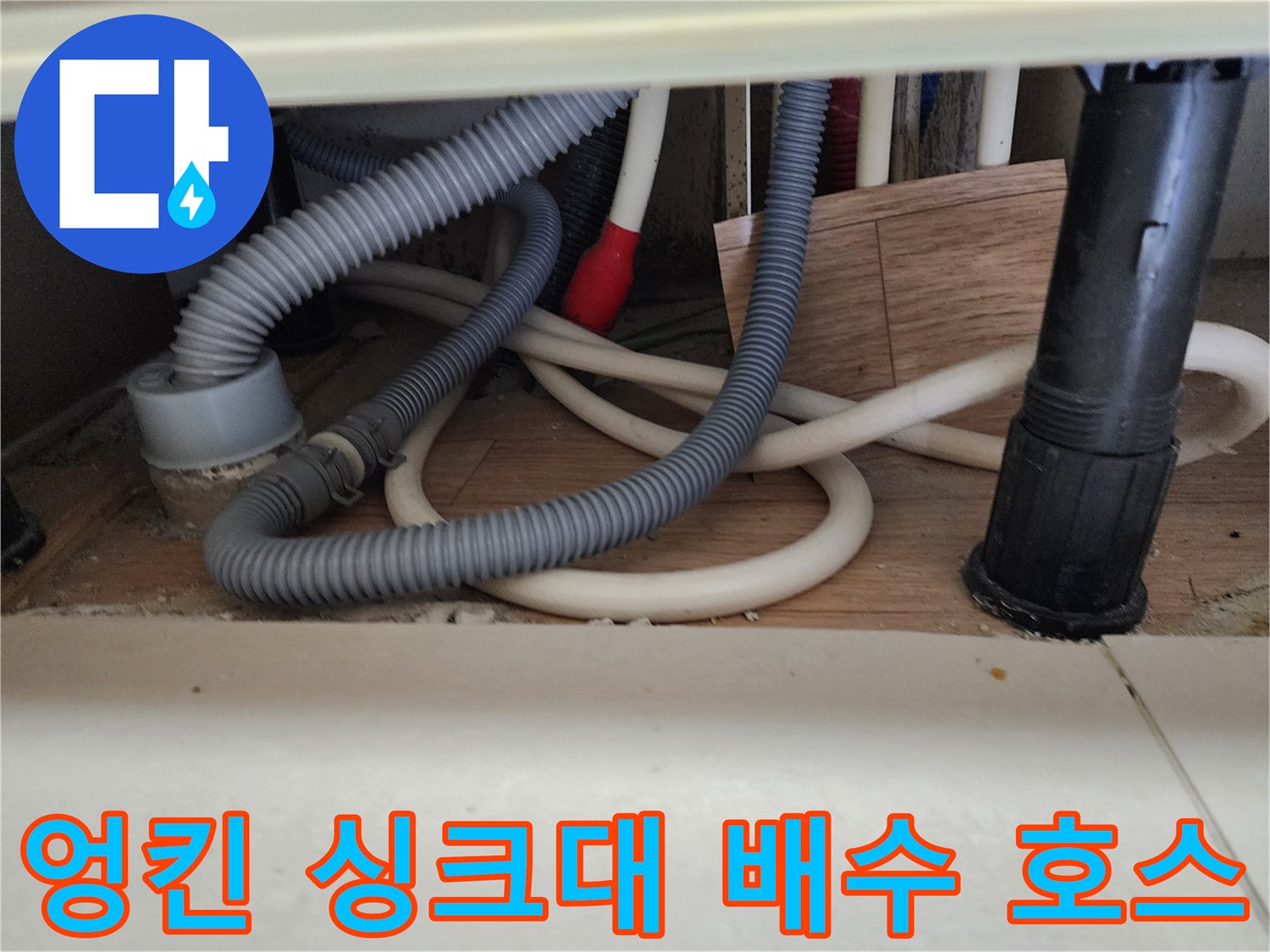 주방 하단부에 복잡하게 연결된 회색 주름관과 검은색 배관