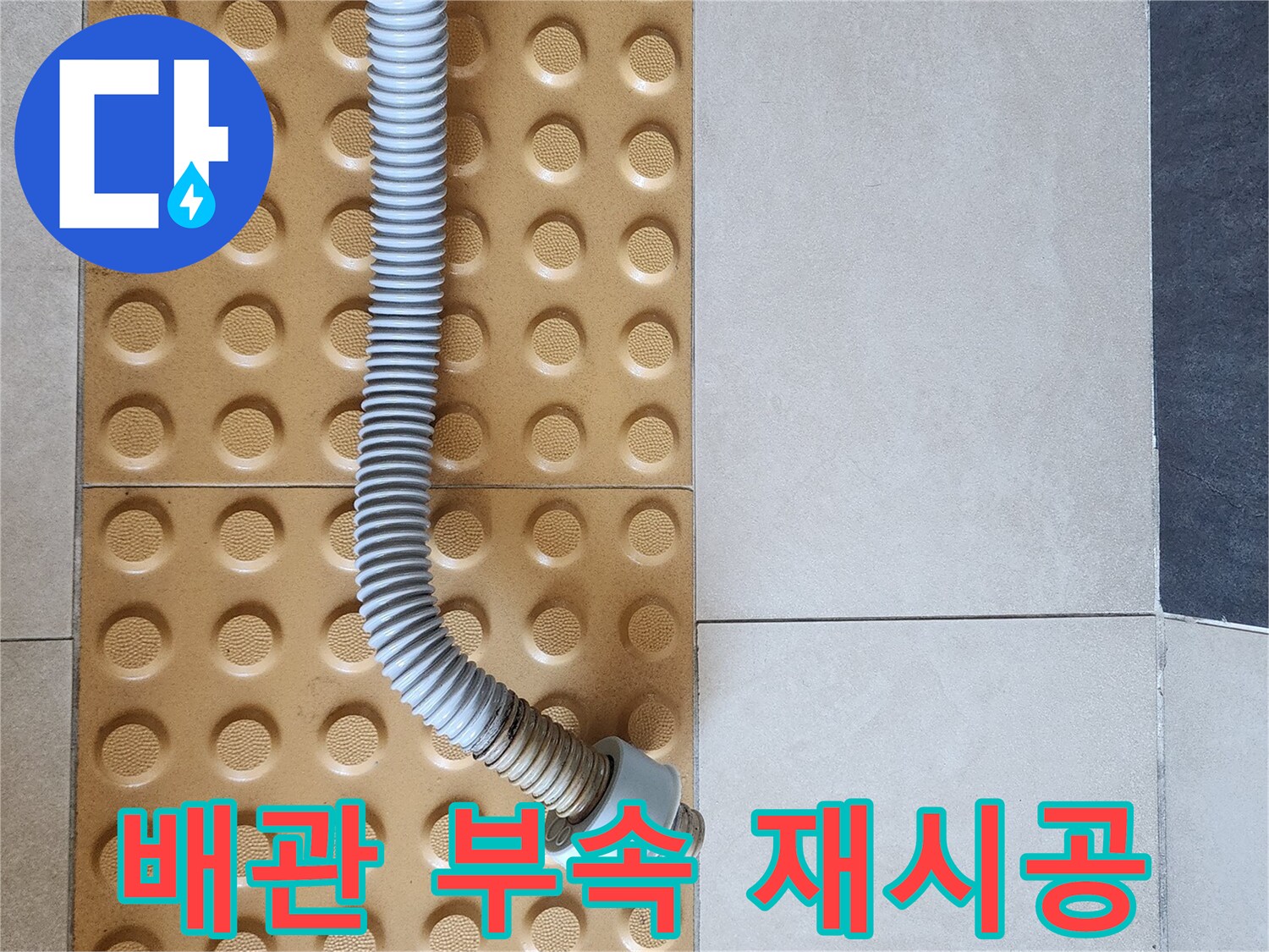 바닥 타일 위에 설치된 변기용 배관 연결 부위와 유연한 호스입니다.