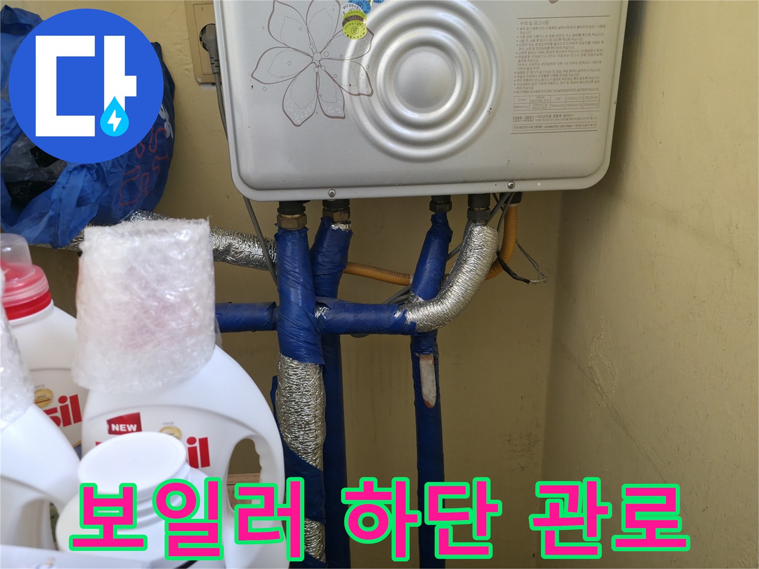 보일러 아래 연결된 파란색 수도 배관과 은박 테이프 마감 부위