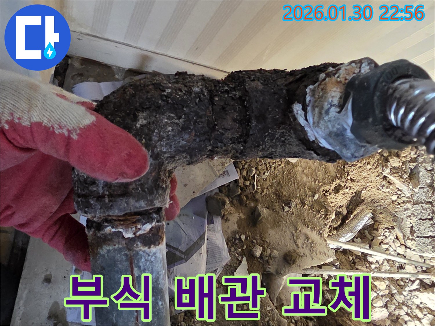 심하게 부식된 수도관 엘보를-전문가가 직접 손으로 들어 확인하는 모습으로-누수 공사의 중요성을 보여줍니다.