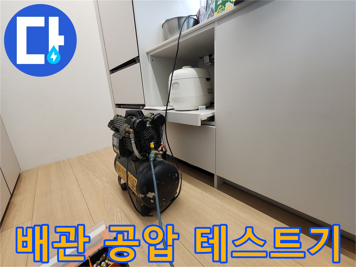 주방 하부장 근처에 설치된 공기 압축기와 배관 점검용 호스