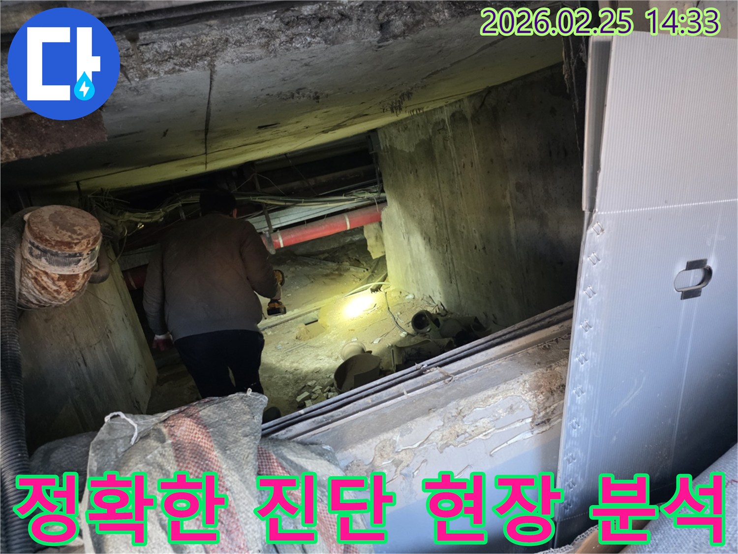 누수 전문 엔지니어가-어둡고 좁은 현장에서-손전등을 비춰가며-누수의 정확한 원인을-진단하기 위해-배관을 면밀히 분석하는 모습입니다.