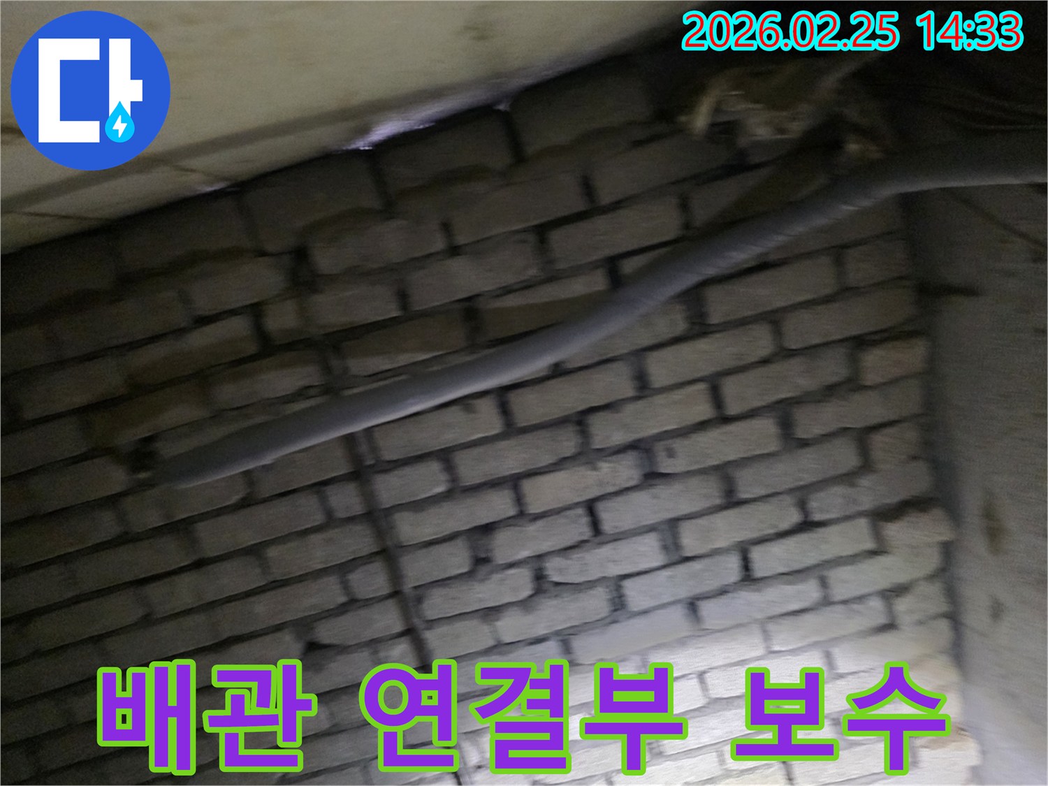어두운 벽돌 벽면을 배경으로-단열된 배관의 연결부에서-누수 보수 작업을 위해-정밀하게 검사되는 현장 모습입니다.