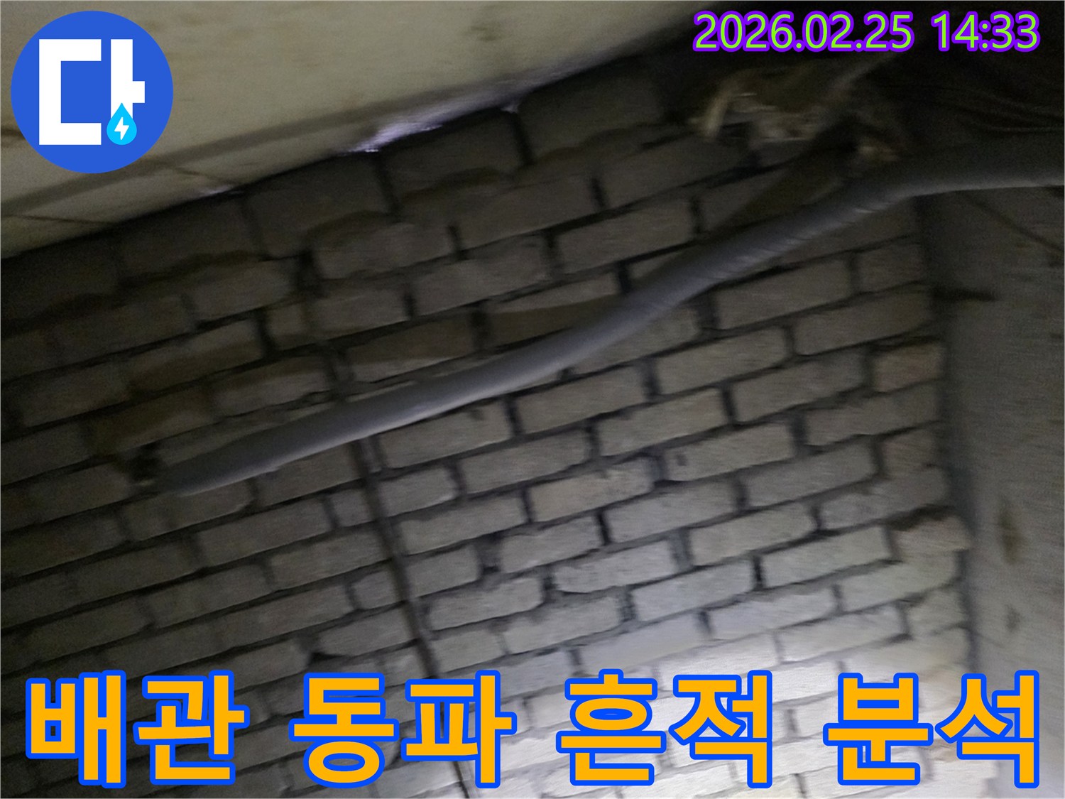 어두운 벽돌 벽면을 배경으로-단열재로 감싸인 배관에서-동파로 인한 누수 흔적을-확인하기 위해 촬영된 현장 이미지입니다.