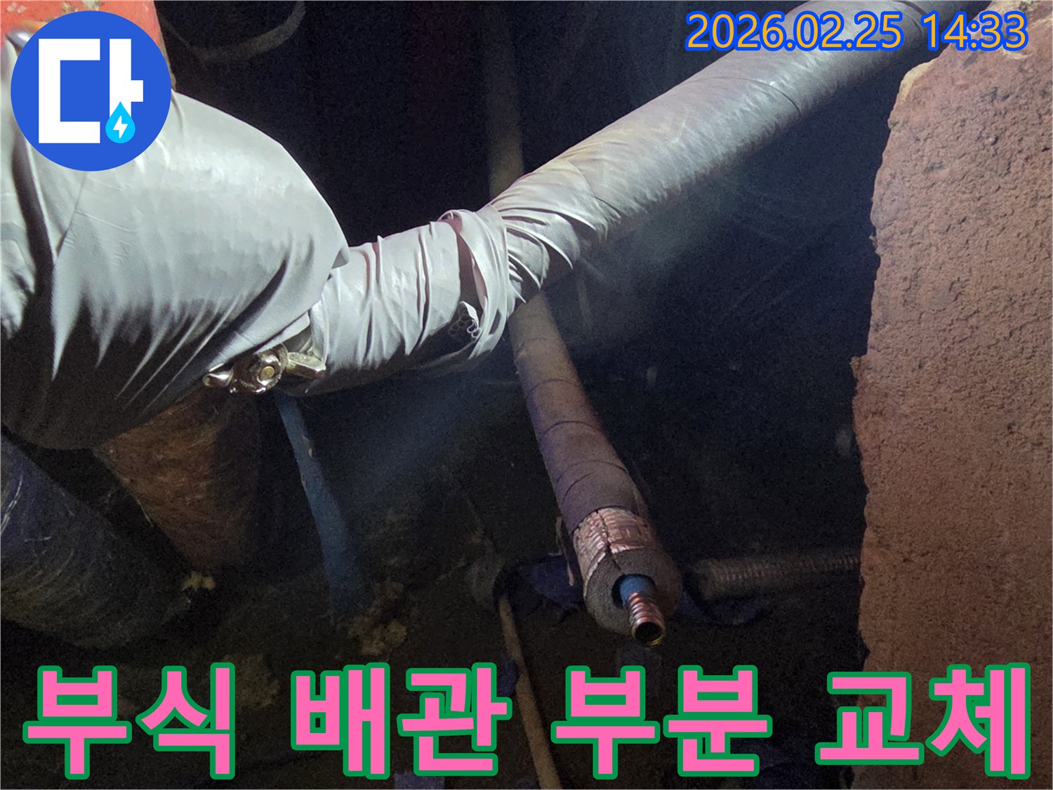 어두운 작업 공간에서-장갑을 낀 손이-부식된 배관의-손상 부위를-새로운 배관으로-부분 교체하는-모습을 담고 있습니다