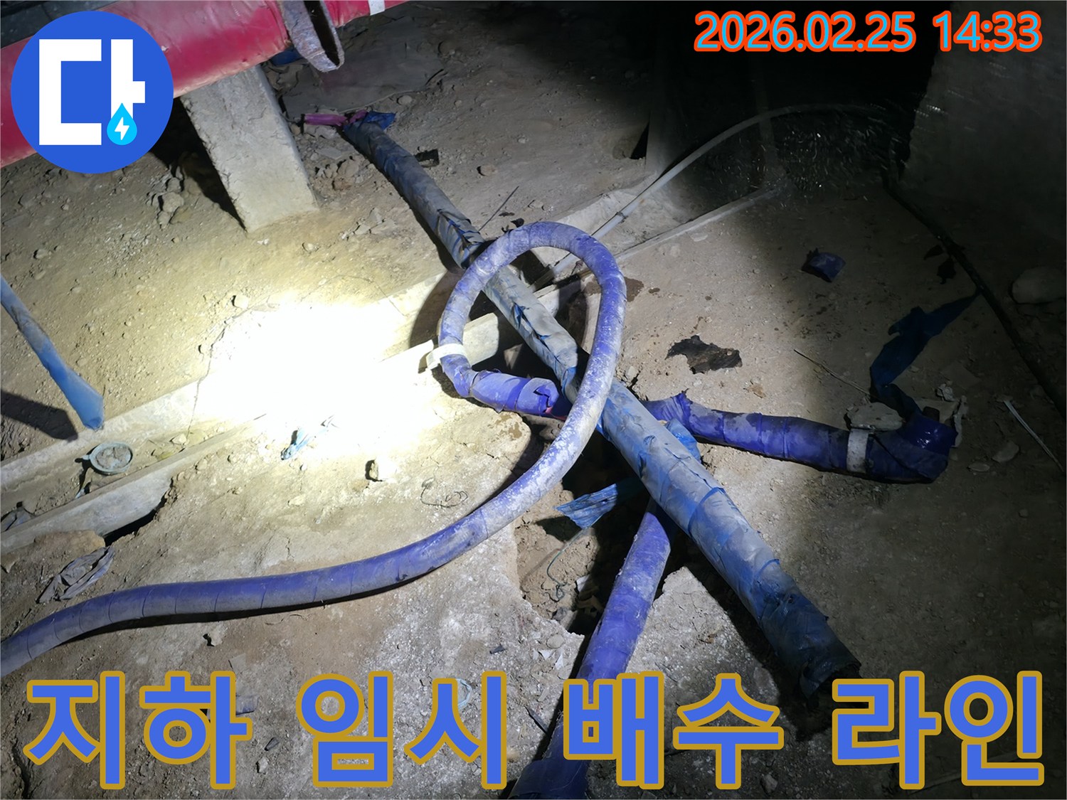 어둡고 복잡한 지하 공간에-임시 배수 라인을 설치하여-누수 현장을 관리하는 모습입니다