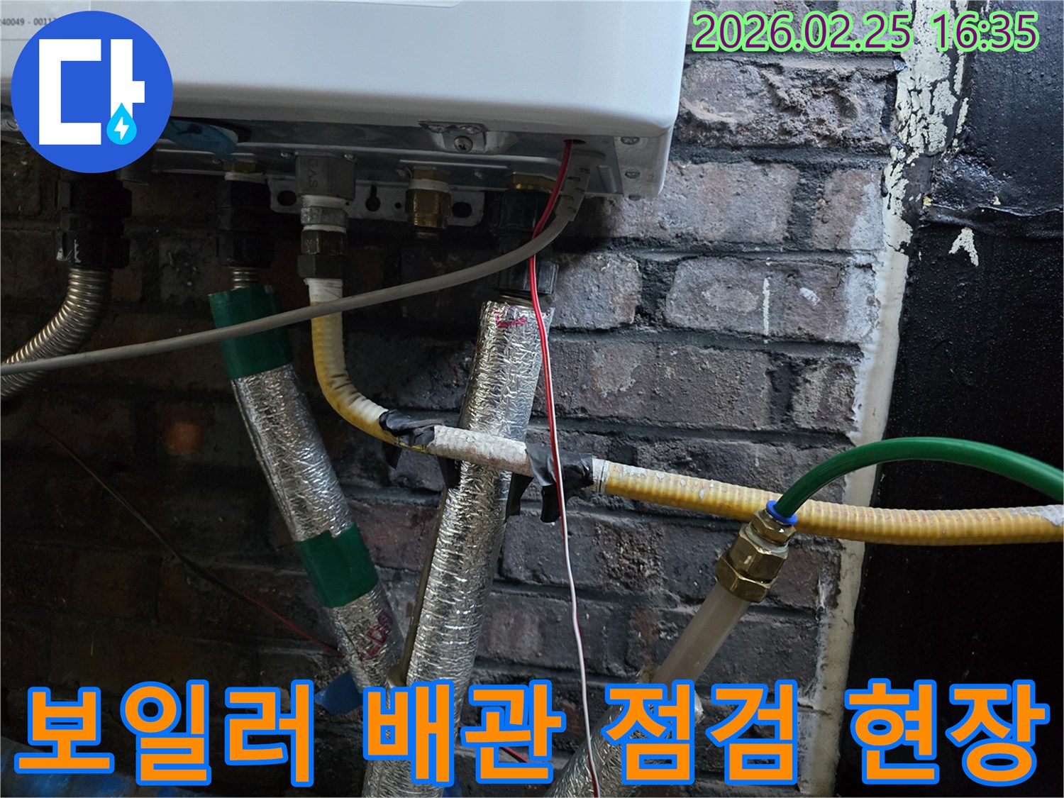 이 이미지는-벽에 설치된-보일러 하단부의-복잡한 배관 연결부와-전선-그리고-은색 단열재로-감싸진-파이프들을-자세히-보여줍니다.