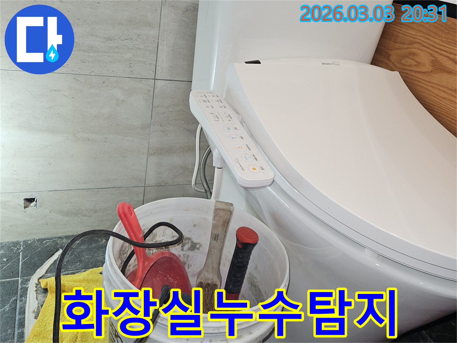 이 이미지는-화장실에서 누수 탐지 및 수리 작업을 위해 준비된-다양한 공구들이 담긴 양동이와-변기 주변의 모습을 보여줍니다.