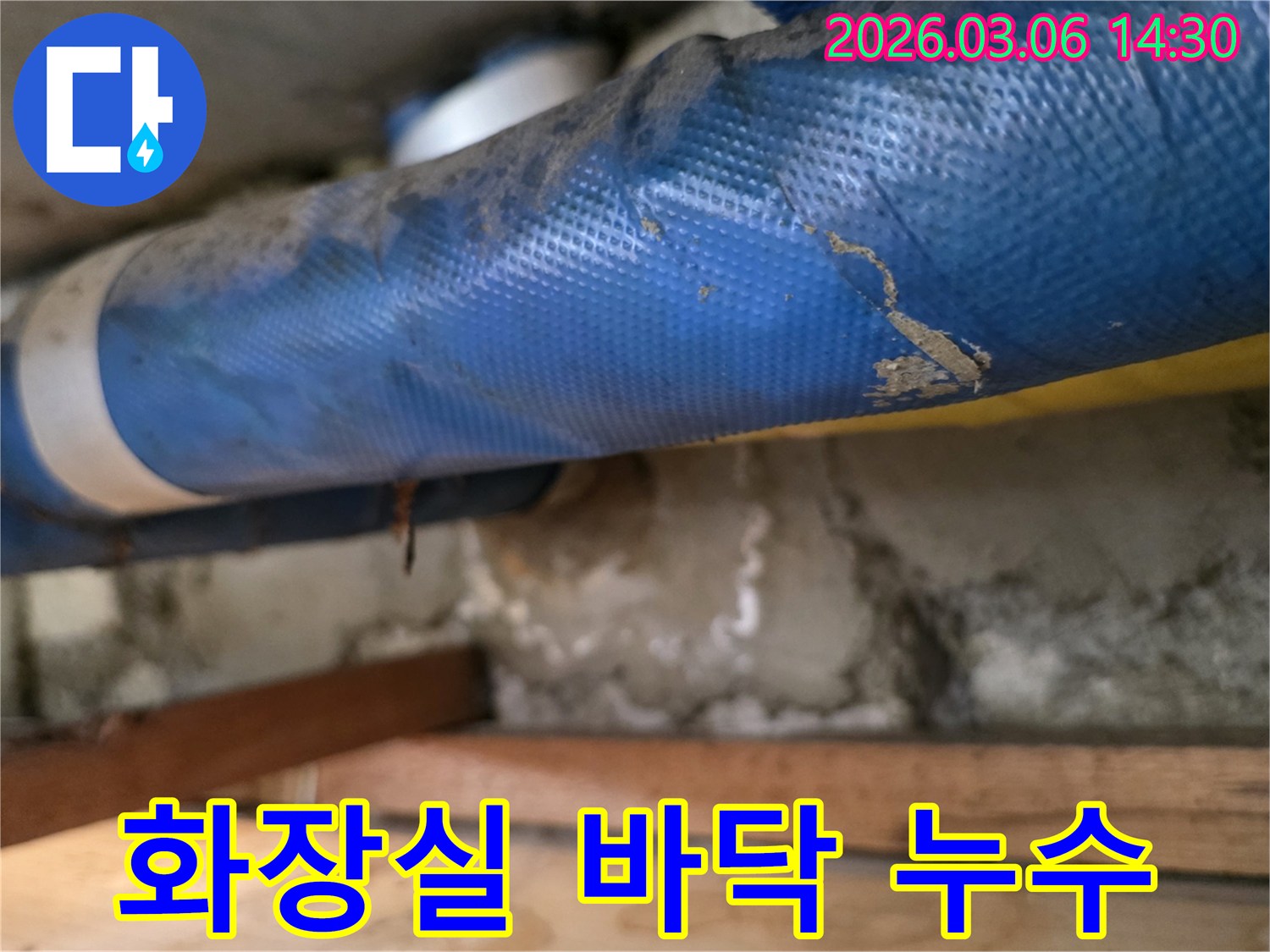 아파트 화장실 바닥-파란색 배관과-젖은 콘크리트 벽면-그리고 나무 지지대를-꼼꼼히 점검하는 모습
