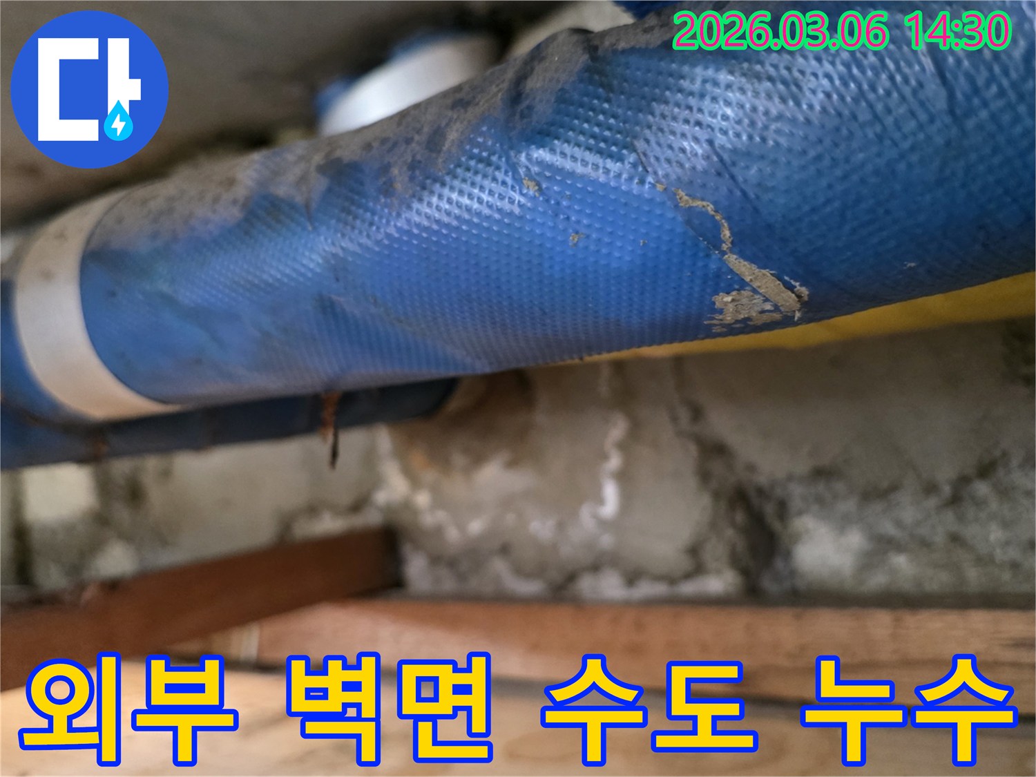주택 외부 벽면-파란색 수도 배관과-심하게 젖은 콘크리트-그리고 나무 지지대를-꼼꼼히 점검하는 장면