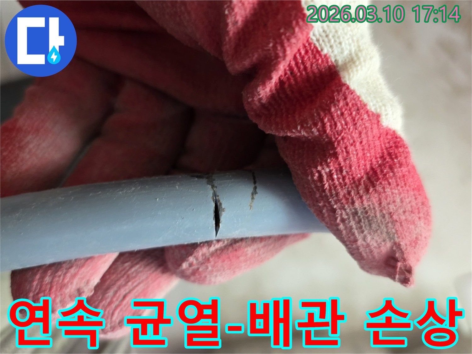 작업용 장갑을 낀 손이-여러 곳이 균열된 배관을 잡고-누수 상황을 보여줍니다