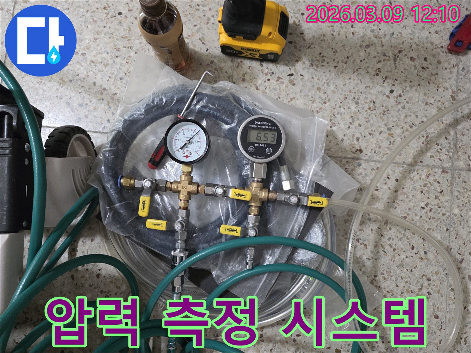 누수 탐지를 위한 배관 압력 측정 시스템의-핵심 부품인 게이지와-연결 호스-밸브들이 바닥에 놓여 있습니다.