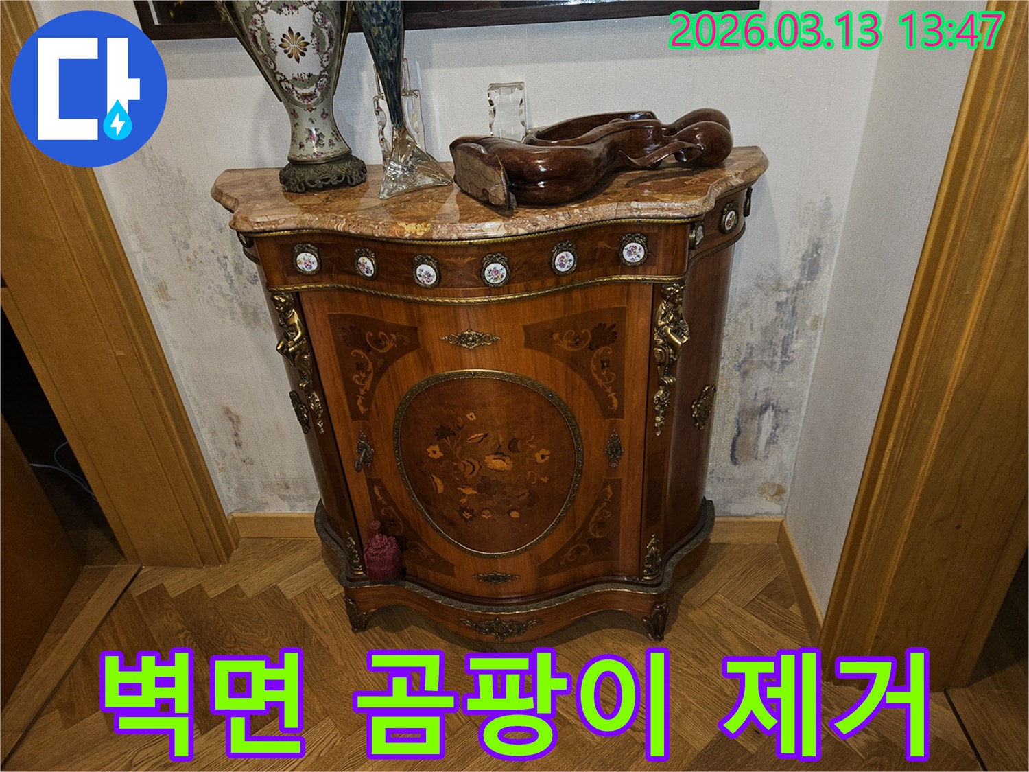 고풍스러운 콘솔 가구 뒤-벽에 발생한-누수로 인한-벽지 변색과-곰팡이 흔적을 보여주는 사진