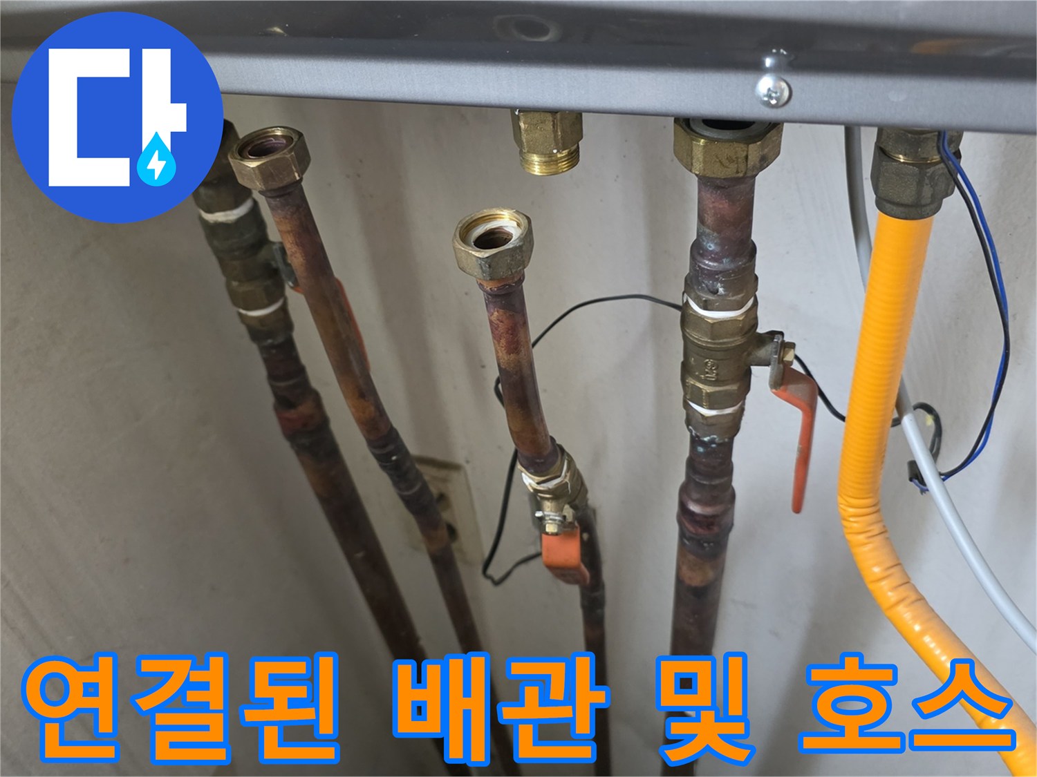 보일철 하단에 복잡하게 연결된 금속 배관과 노란색 급수 호스입니다.