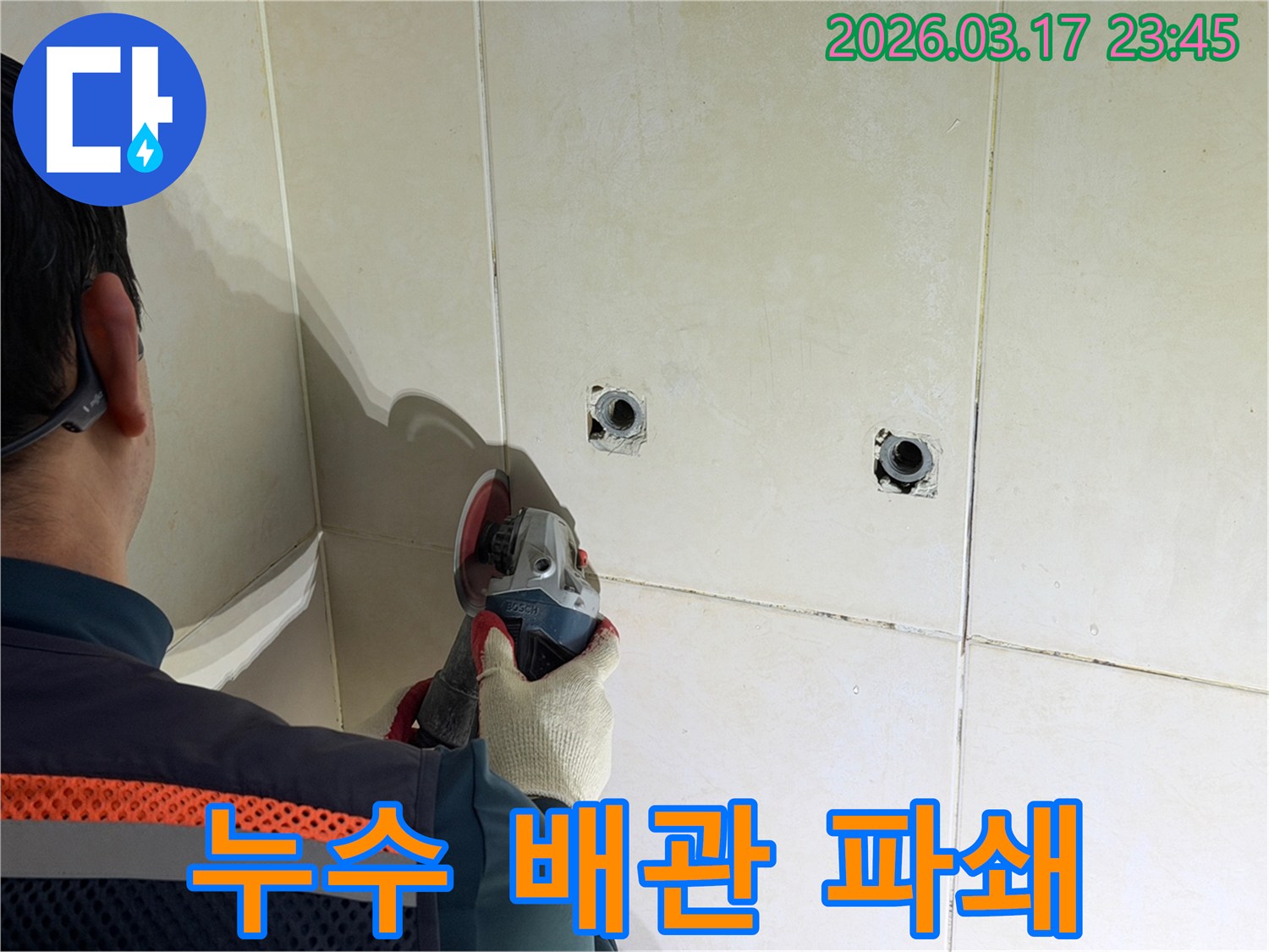 누수된 배관을-노출시키기 위해-전문가가-타일 벽면을-그라인더로-조심스럽게-파쇄하고-있습니다