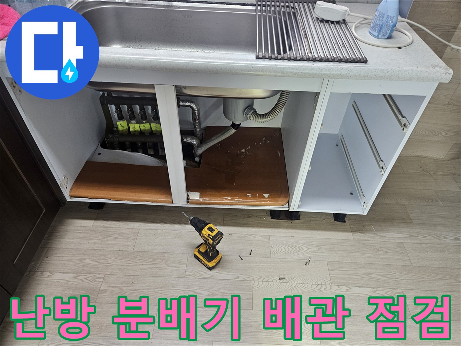 싱크대 하부장 내부에 노출된 난방 분배기와 연결 배관들
