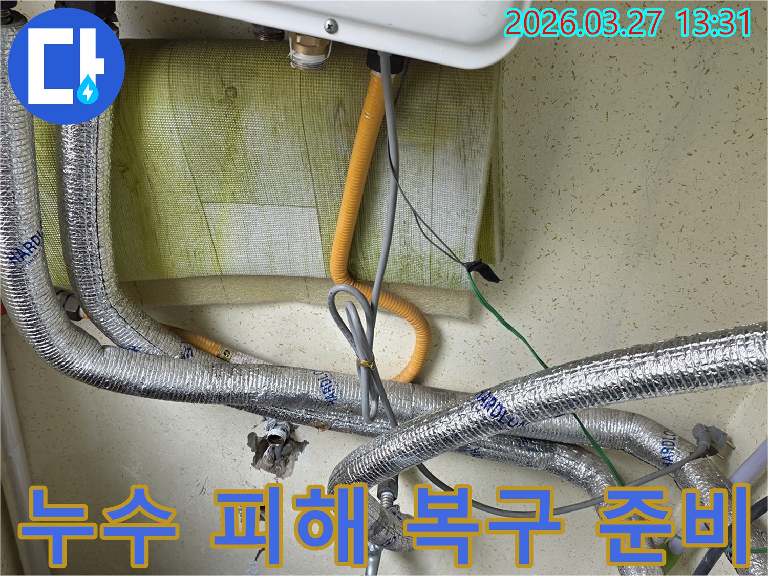 보일러-하단에-연결된-배관-주변의-벽면-손상-흔적을-보여주며-누수-피해-복구를-위한-현장-조사-중입니다.