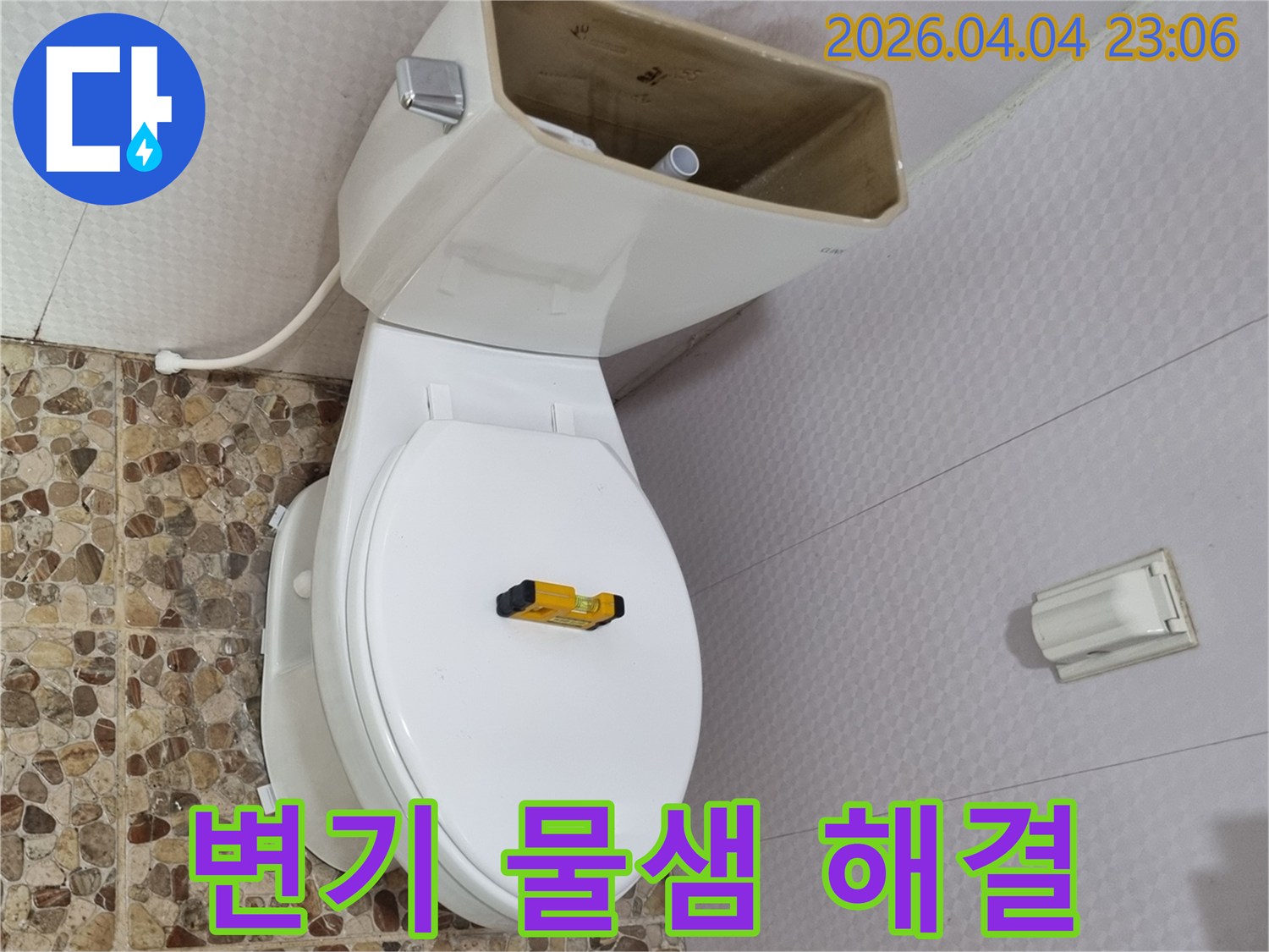 변기 물탱크가 열려 내부 부품이 노출된 상태로-수평계가 변기 시트 위에 놓여-물샘 해결을 위한 점검이 진행 중입니다