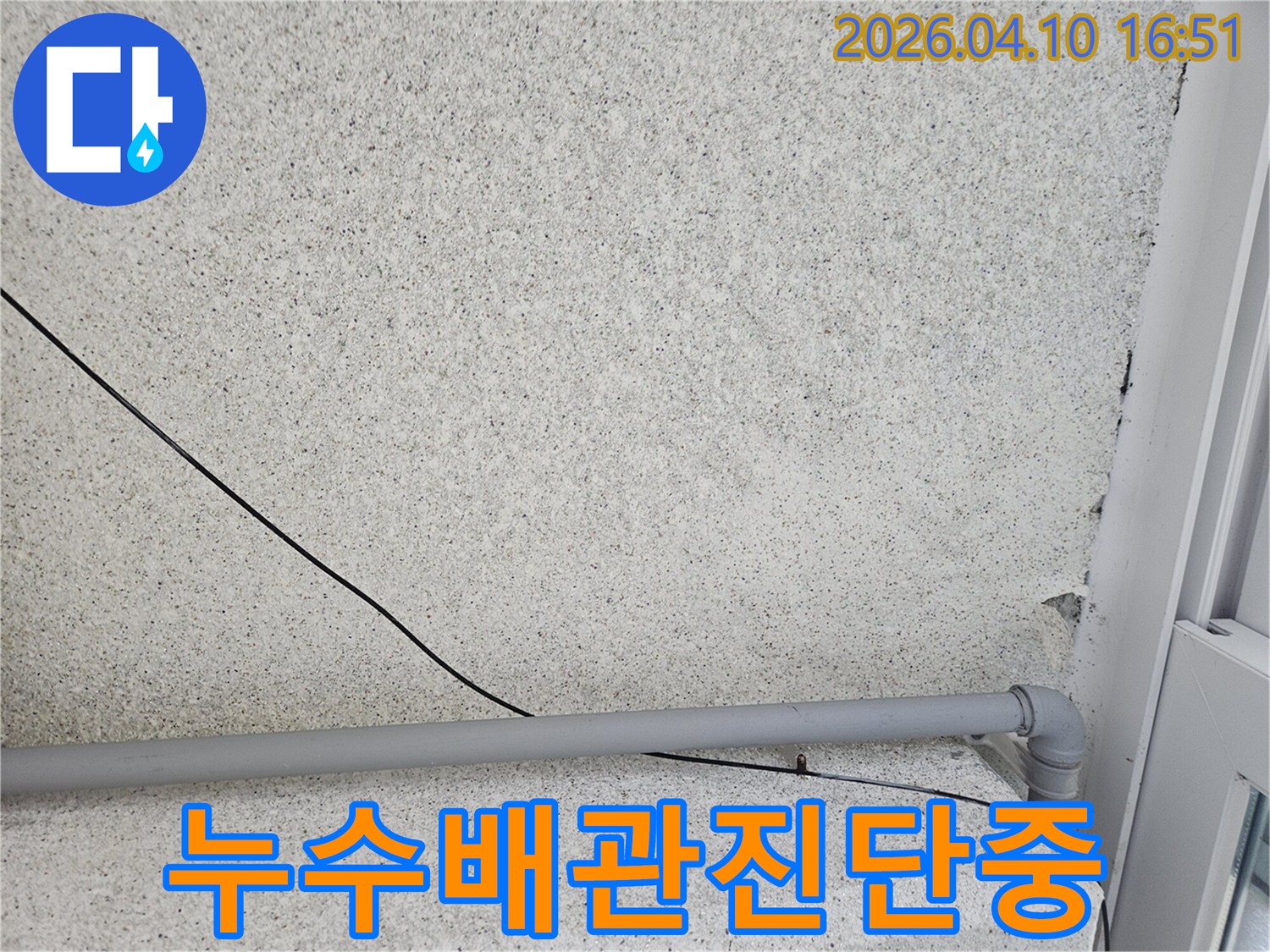 회색 외벽에-설치된 회색 배관과-검은 전선이-누수 여부를-확인하기 위해-점검되고 있는-사진입니다