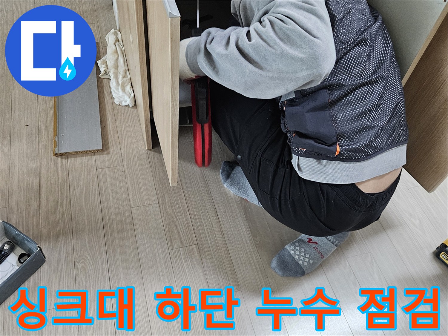 싱크대 밑 공간에서 배관의 결함을 찾고 있는 작업자의 모습