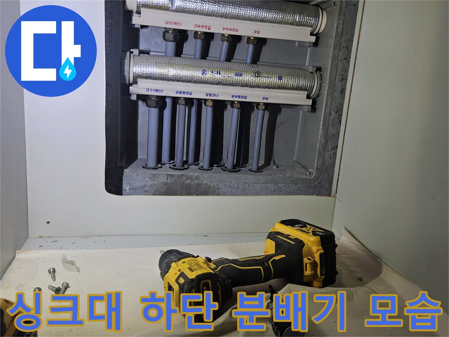 싱크대 아래쪽 좁은 공간에 설치된 금속제 분배기와 배관들입니다.