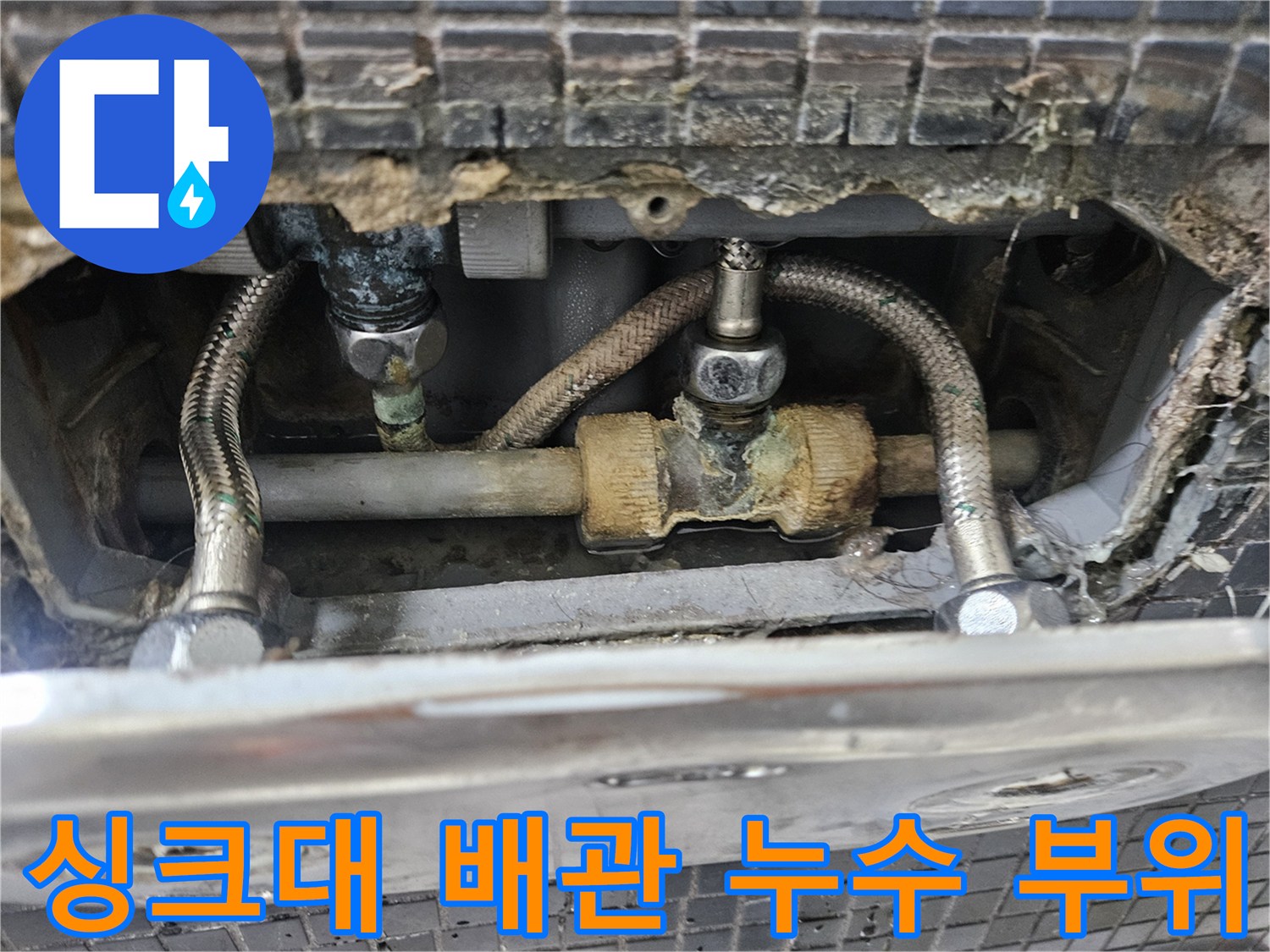 주방 싱크대 하부장 내부의 노후된 금속 배관과 연결 부위 모습
