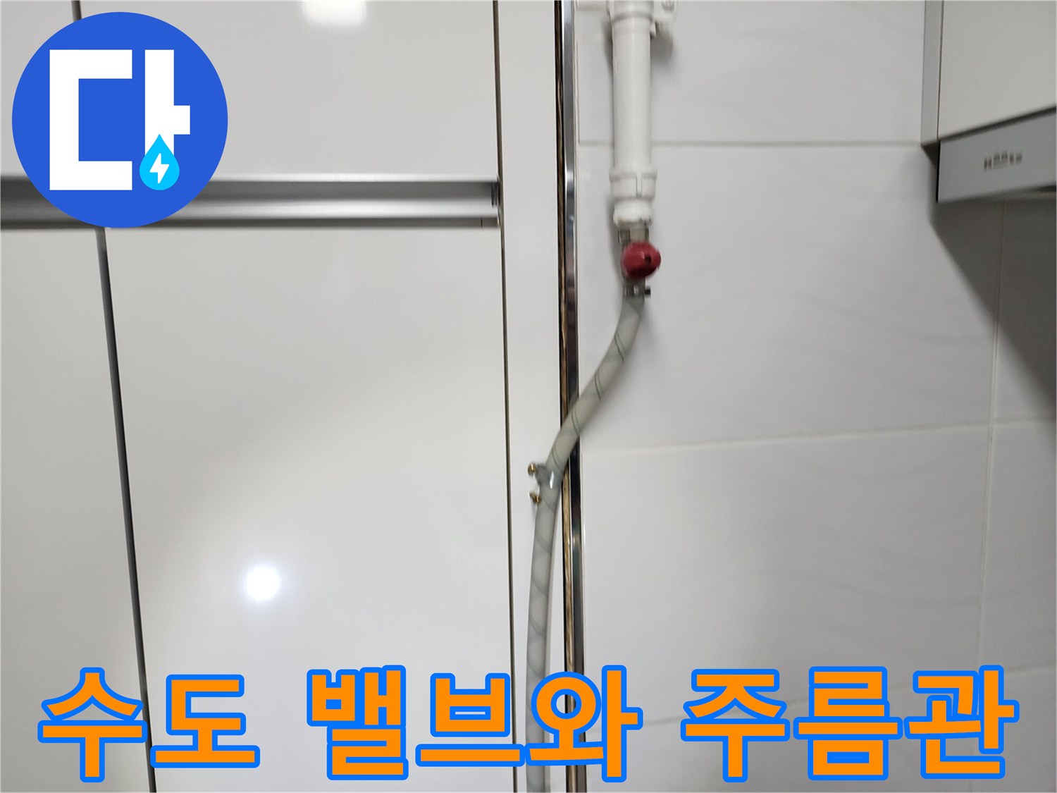 타일 벽면에 설치된 붉은색 수도 밸브와 연결된 은색 배관