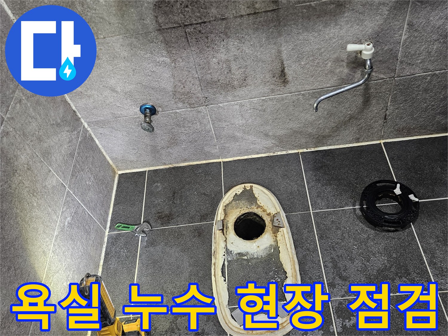 변기가 제거된 욕실 바닥의 배수구와-주변 타일에 나타난 누수 흔적을-손전등으로 밝혀 누수 원인을 분석하기 위해 현장을 점검하는 모습입니다.