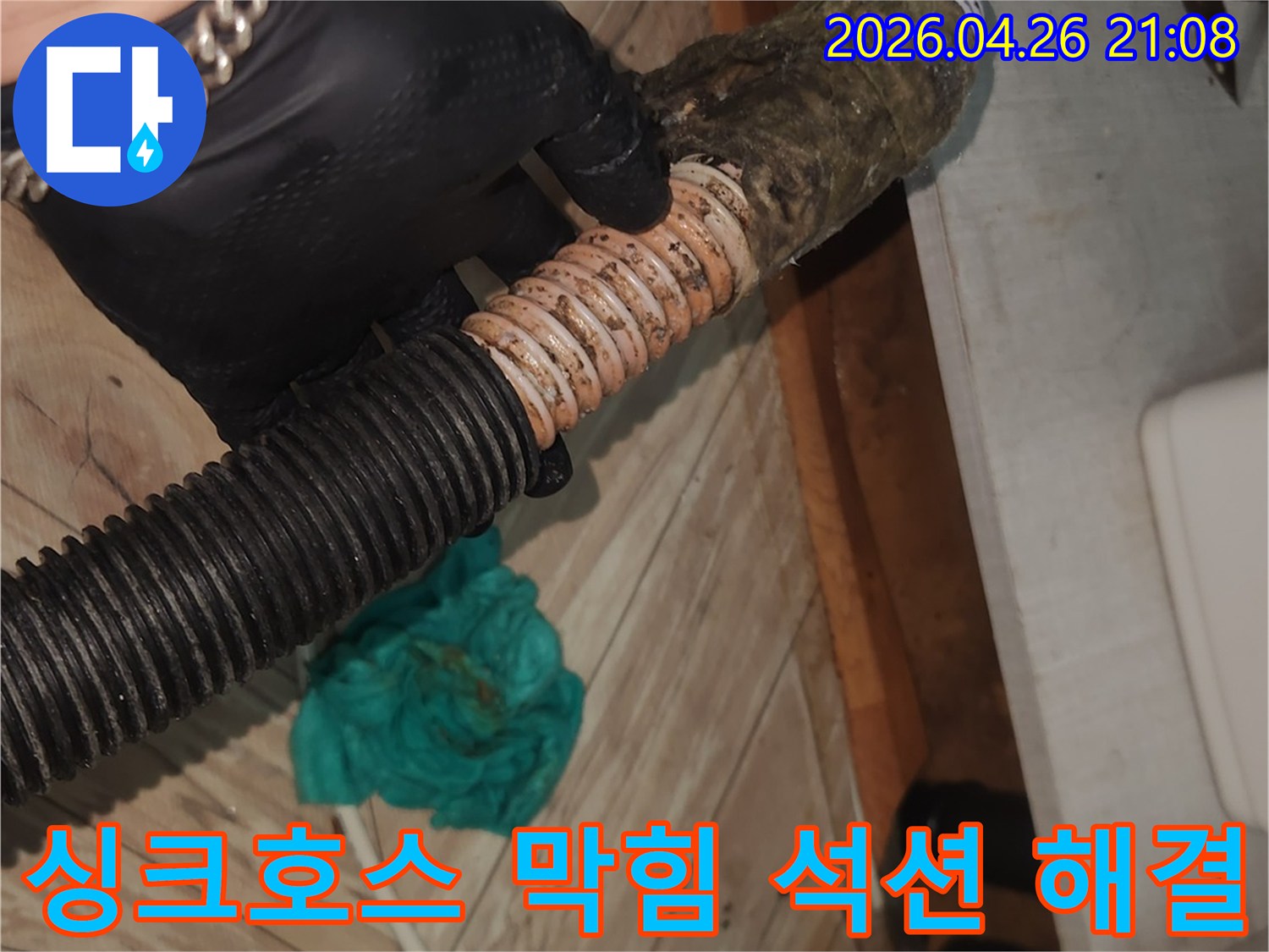 검은 장갑을 낀 엔지니어가-이물질로 막힌 싱크대 배수 호스를-석션 장비로 깨끗하게 청소하는 모습