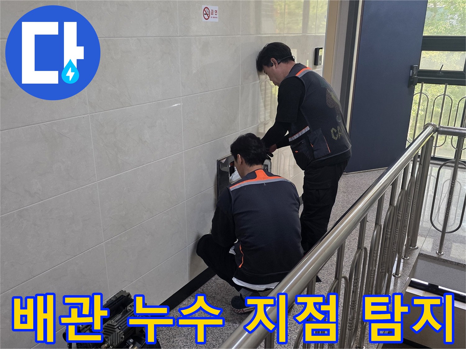 두 명의 전문 기술자가 건물 벽면 내부의 배관 누수 의심 지점을 첨단 장비로 정밀하게 탐지하고 있습니다-정확한 원인 파악을 위한 집중적인 작업입니다.