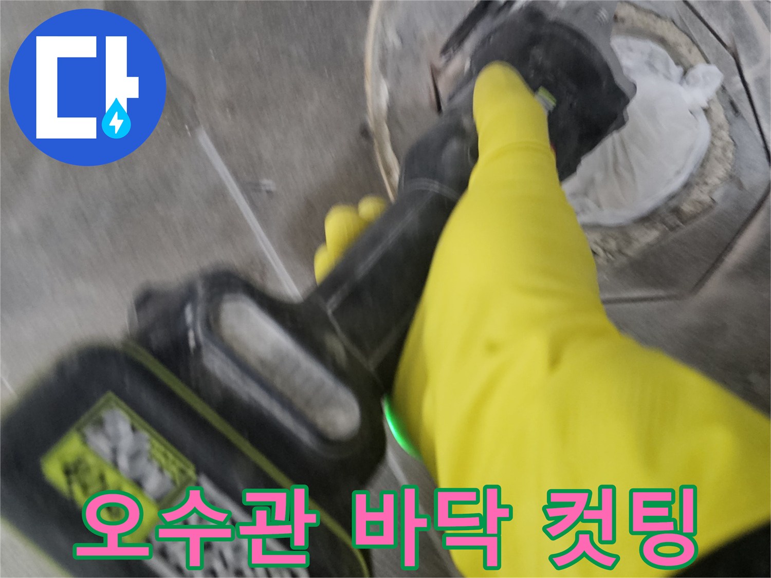 노란색 안전 장갑을 착용한-기술자가-전동 공구를 사용하여-오수관 주변의 바닥 타일을-정교하게 컷팅하여-배관을 노출시키는 현장입니다.