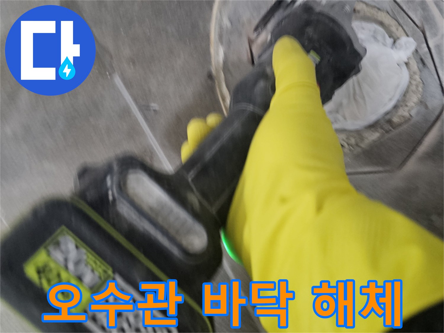 노란색 안전 장갑을 착용한-기술자가-전동 공구를 사용하여-오수관 주변의 바닥 타일을-정교하게 해체하는 현장입니다.