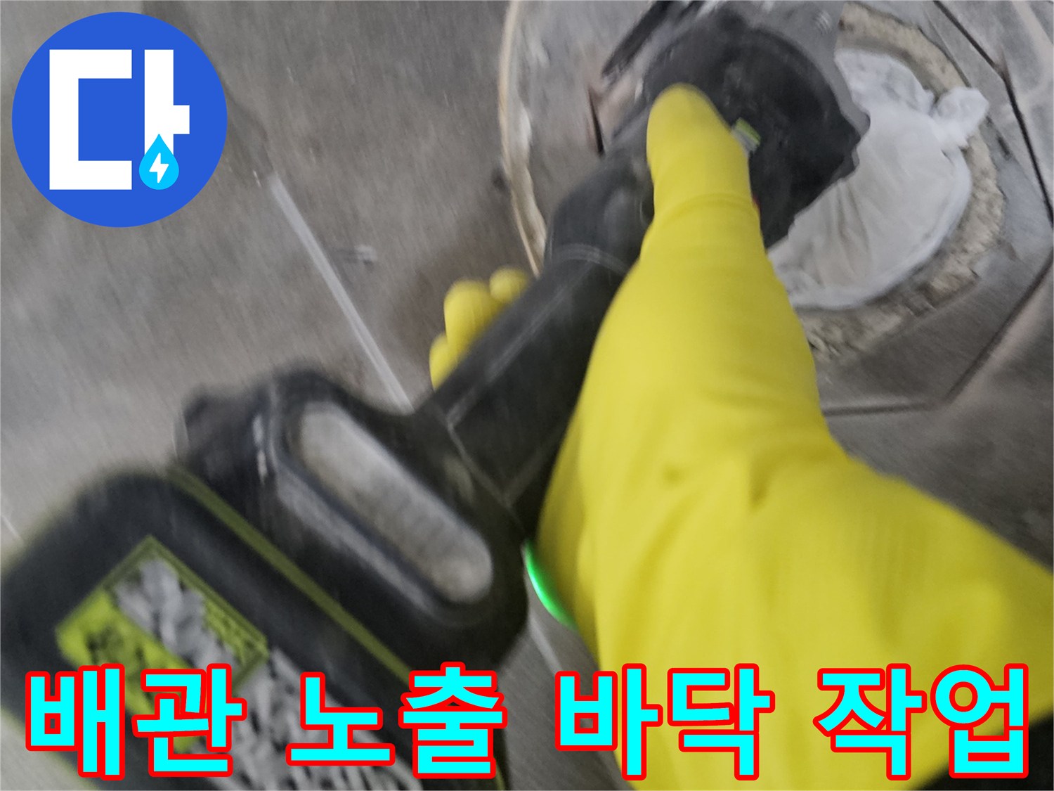 노란색 작업 장갑을 착용한-전문가가-전동 공구로-오수 배관 주변의 바닥 타일을-세심하게 제거하여-배관을 노출시키는 과정입니다.