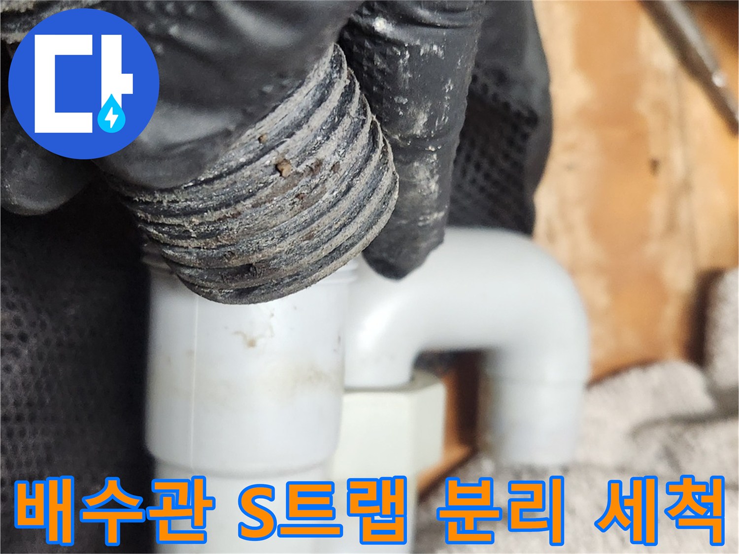 작업자가 검은 장갑을 착용하고-오염된 S트랩 배관을 해체하여-내부 청소를 준비하는 장면입니다