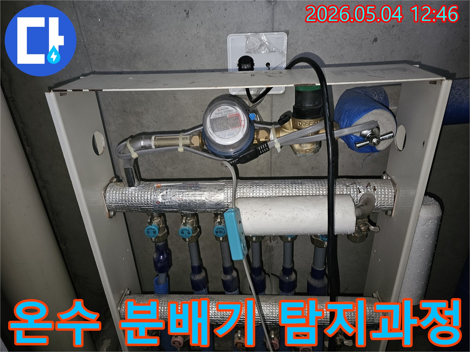 이 이미지는 아파트 온수 분배기에서 누수를 정밀하게 탐지하는 과정을 보여줍니다-다수의 배관과 밸브-유량계가 설치되어 있습니다.