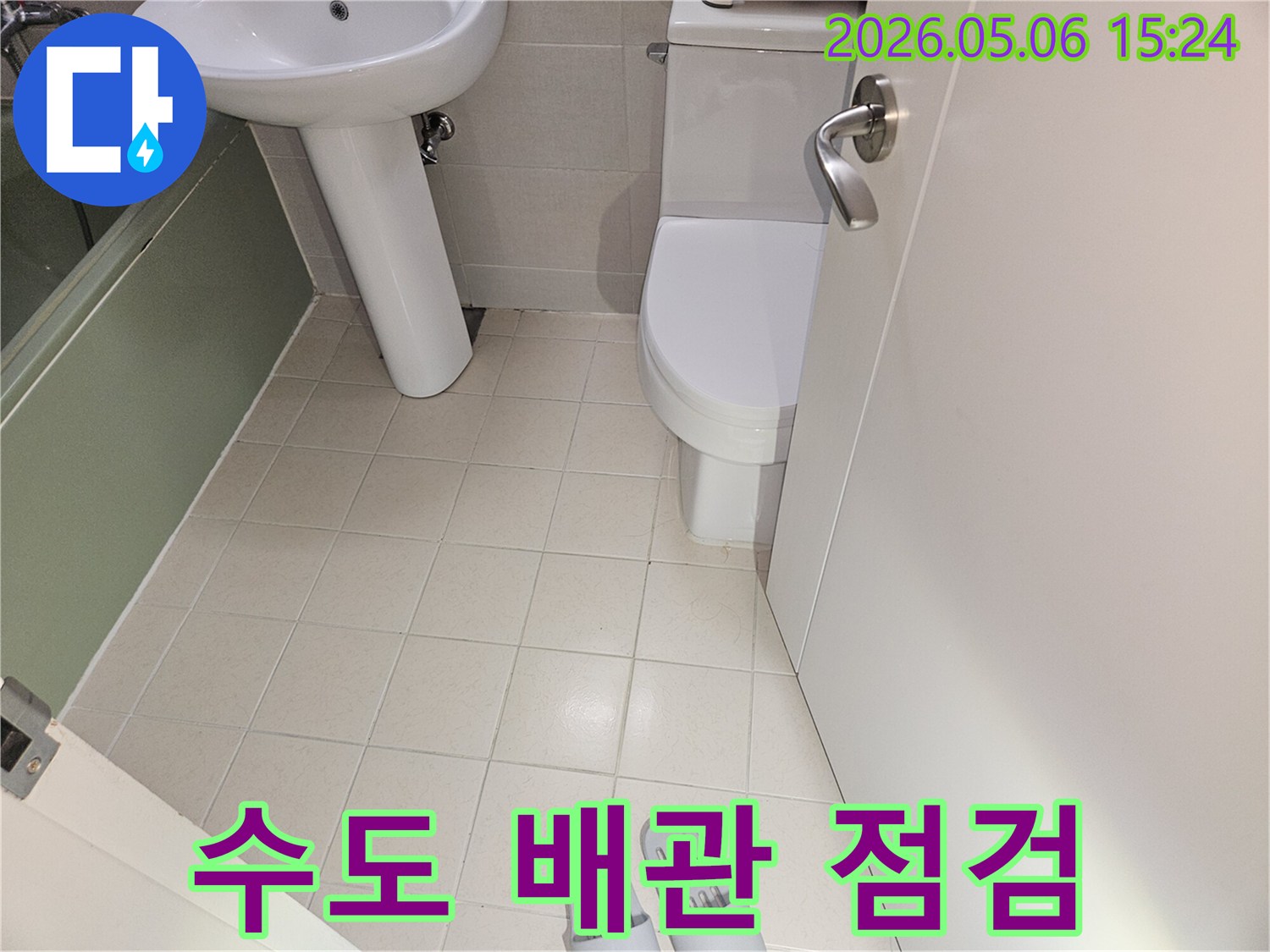 욕실 내부에-설치된-변기와 세면대-그리고 바닥 타일의-전반적인-배치와-상태를-보여주는-사진입니다.