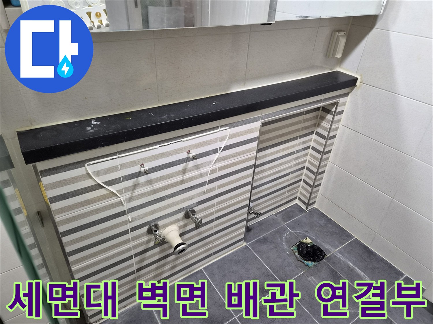 가로 줄무늬 타일 벽면에 설치된 수도 밸브와 하부 배관 모습
